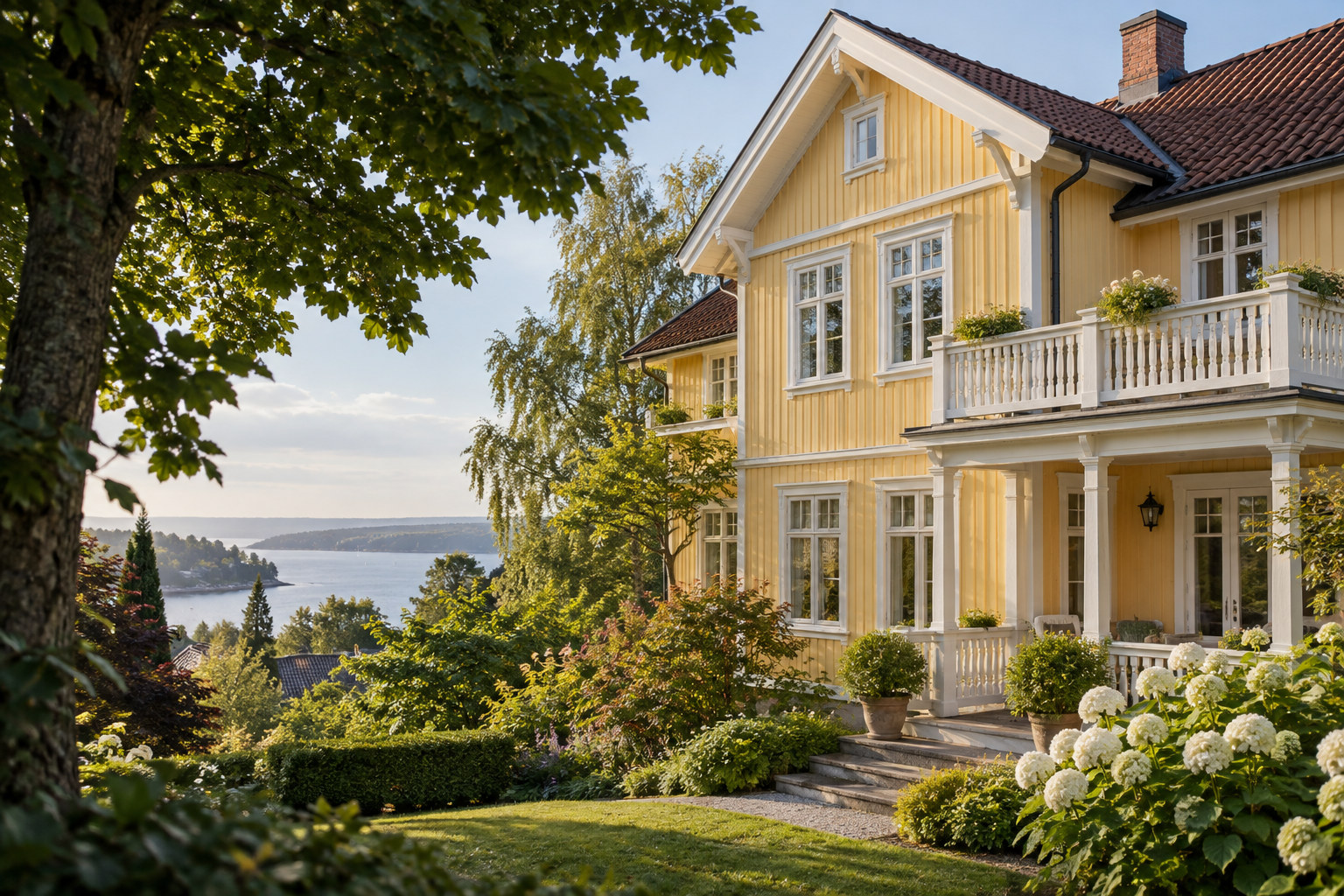 Gul trevilla med hvite detaljer, veranda og frodig hage med utsikt mot fjorden