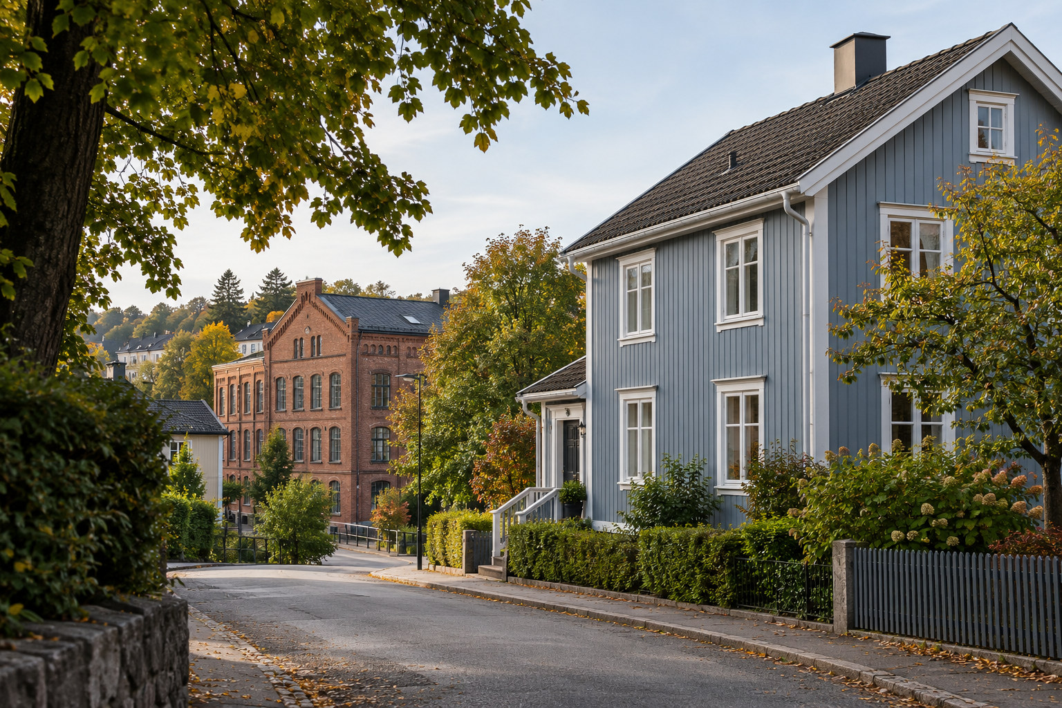 Blågrått trehus med hvite detaljer ved en skrånende gate, med teglbygning og grønne hager i bakgrunnen